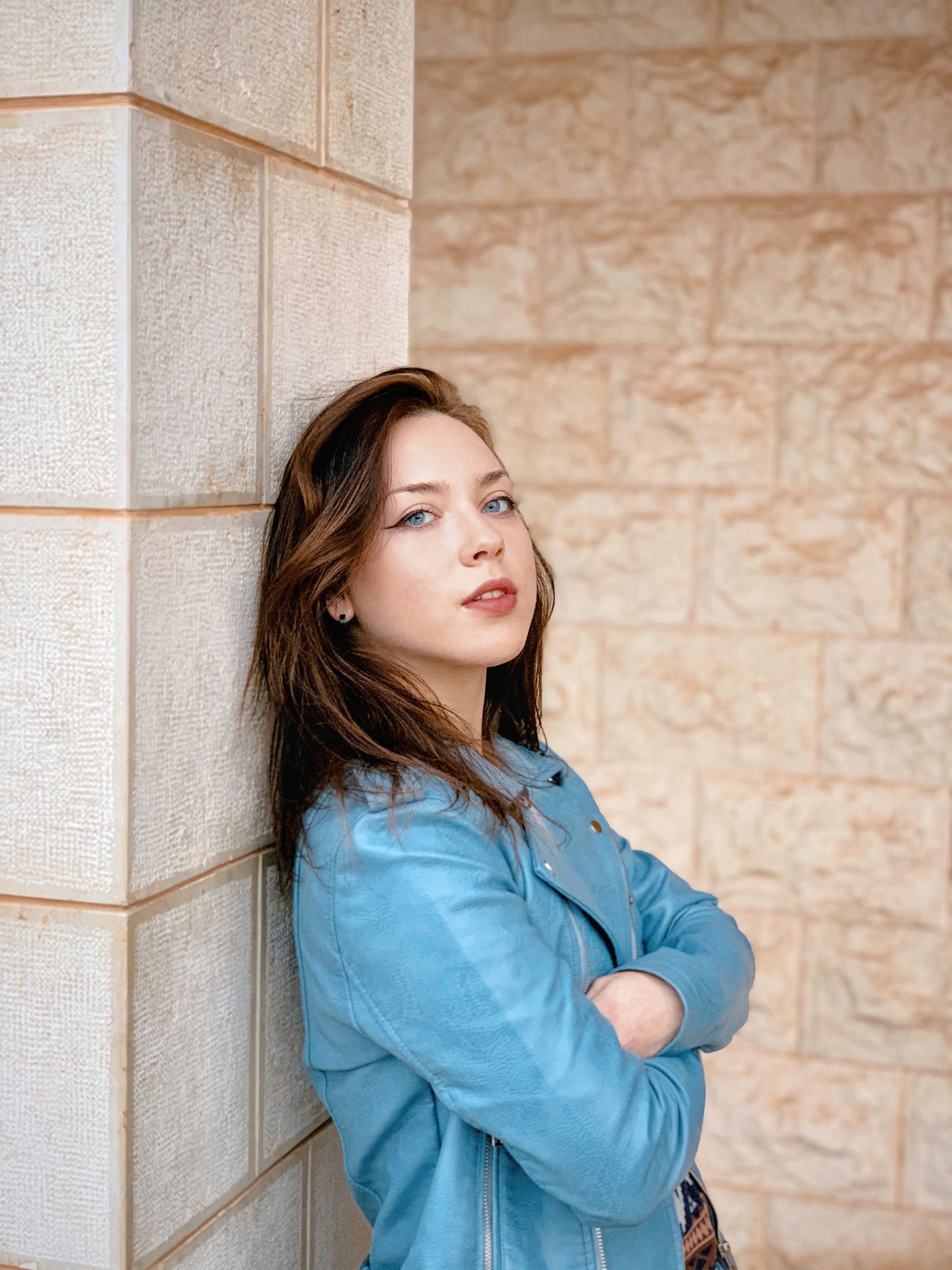 Woman in Blue Long Sleeve Shirt Leaning on Brown Wall · Free Stock Photo