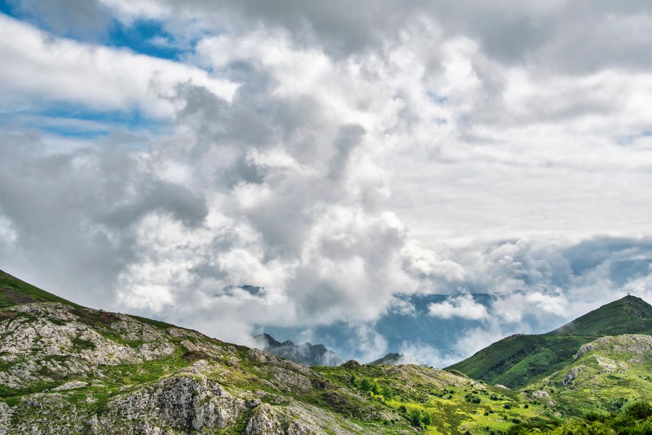 Fotomural Impresionante vista de un paisaje montañoso verde bajo nubes dramáticas y en movimiento.