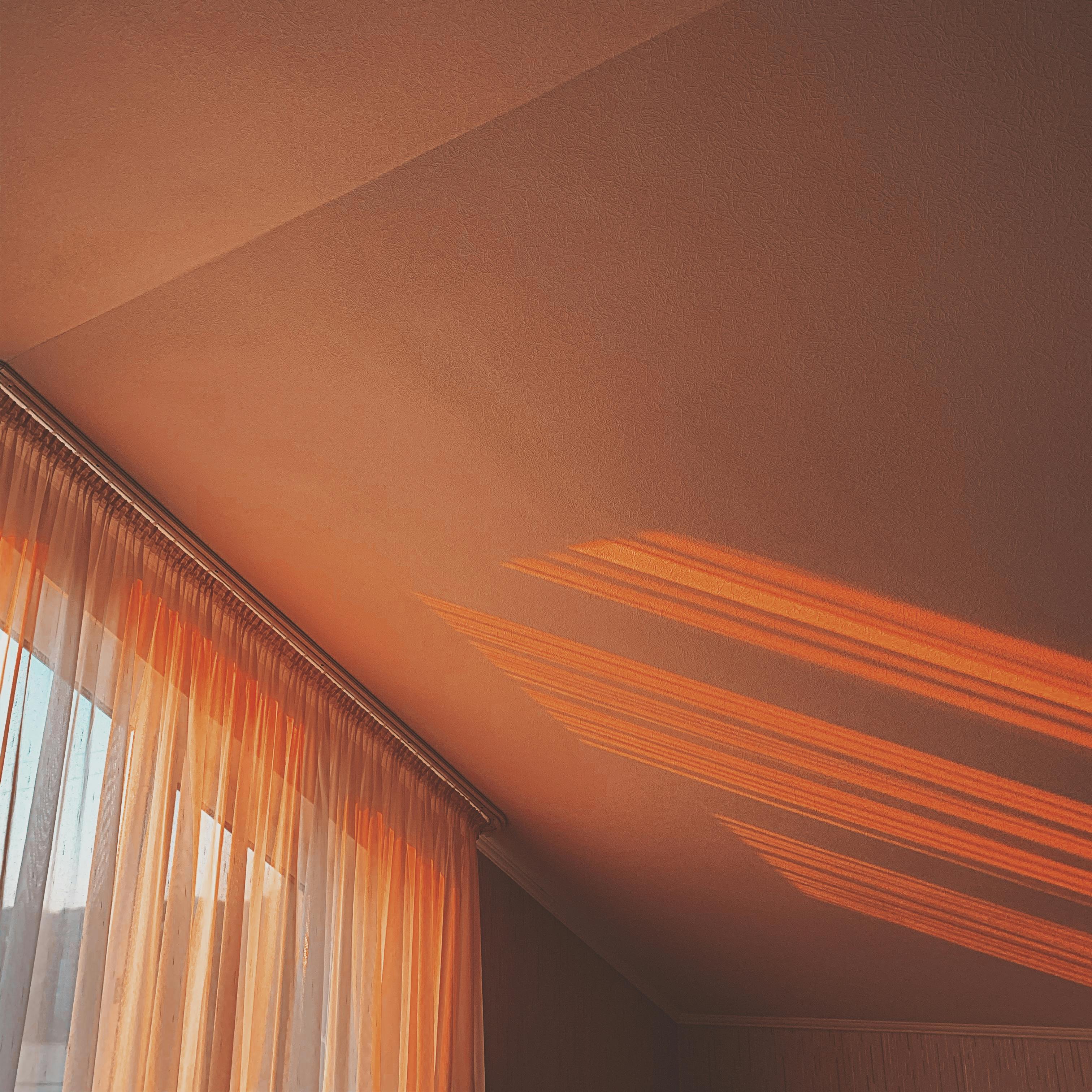 Soft sunlight casts warm shadows through sheer curtains onto a ceiling, creating a cozy indoor ambiance.