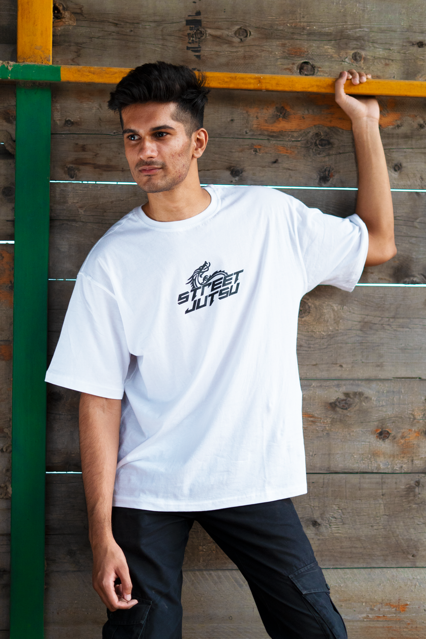 Jovem estiloso com camiseta branca posando contra uma parede de madeira, mostrando moda de rua.