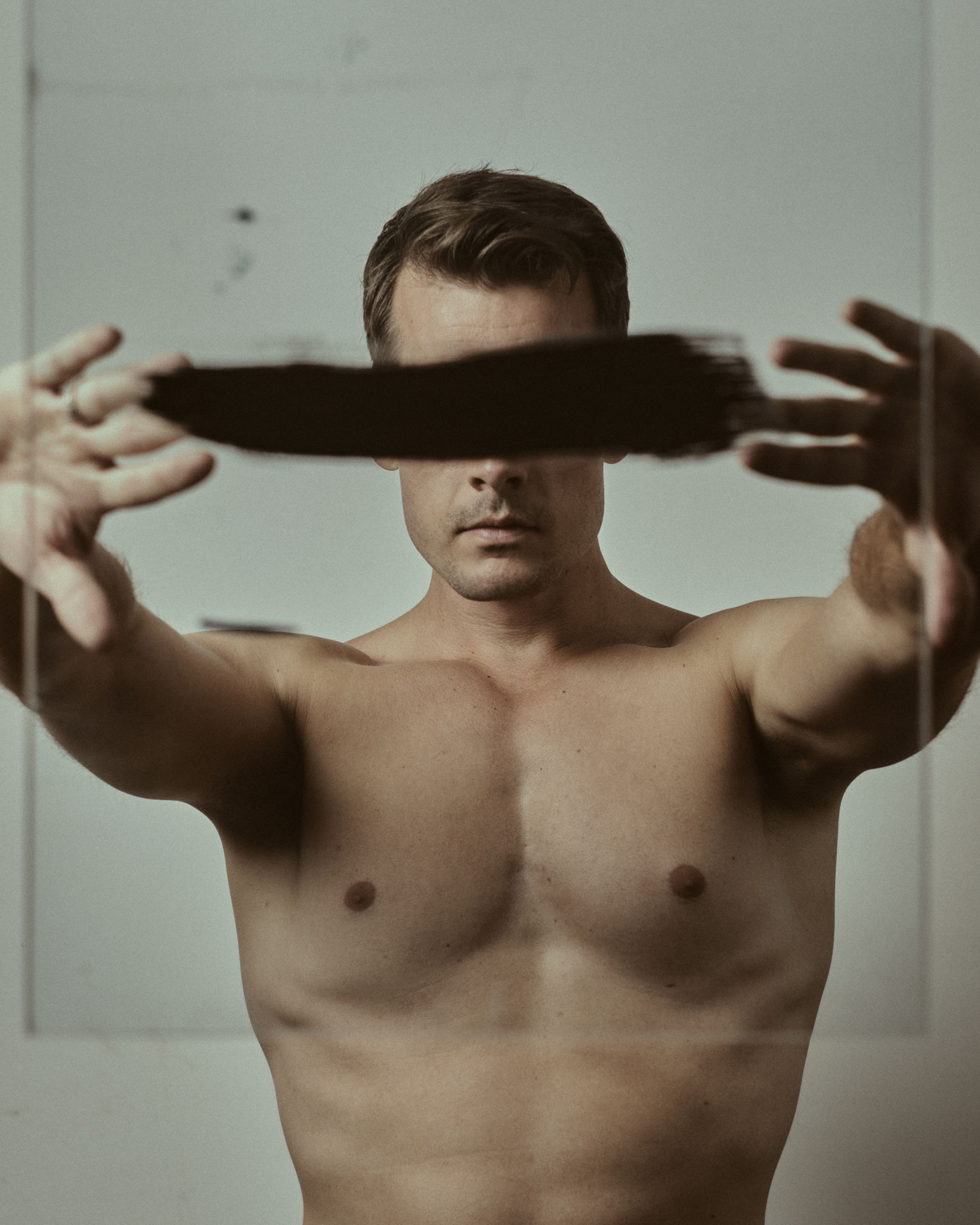 Artistic portrait of a shirtless man indoors with painted eyes, in a conceptual style.