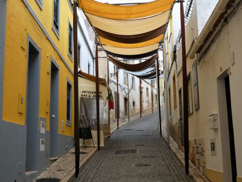 Free Discover the quaint charm of a cobblestone street in Silves, Portugal, with colorful facades and sun shades. Stock Photo