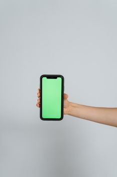 A hand holding a smartphone with a vivid green screen for easy content insertion.