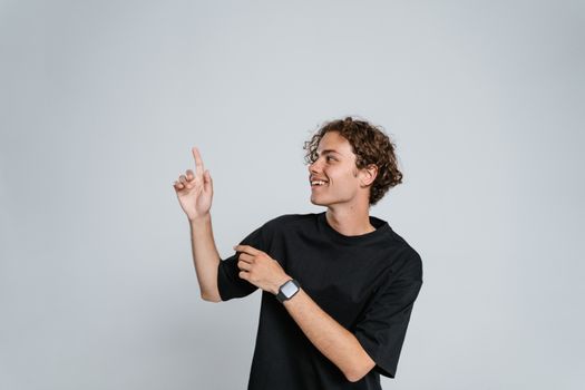 Smiling young man in a black t-shirt pointing upwards against a white background.