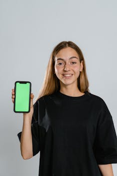 Smiling teenager in black t-shirt holding smartphone with green screen for mockup.