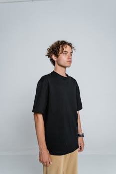 Teenage boy with curly hair posing in black t-shirt and tan pants indoors.