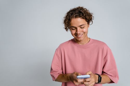 Free Teenager with curly hair smiling down at smartphone in a studio setup. Stock Photo