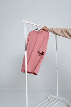 Pink shirt hanging on a white clothing rack in a minimalist setting.