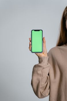 Adult woman holding a smartphone with a green screen, perfect for adding digital content.