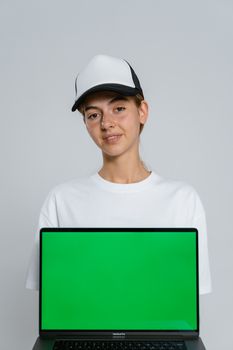 Studio portrait of a woman in casual wear holding a laptop with a green screen.
