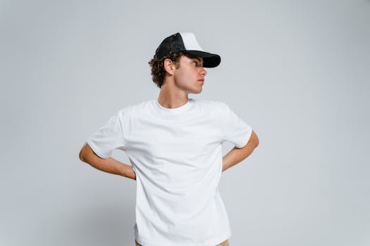 Casual teenager in a white t-shirt and cap looking aside on a plain background.