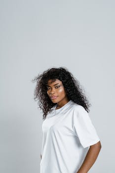Confident woman with curly hair in a studio setting wearing a white t-shirt.