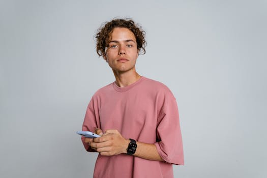 A young adult in a pink t-shirt holding a smartphone with a neutral expression, ideal for tech or lifestyle content.
