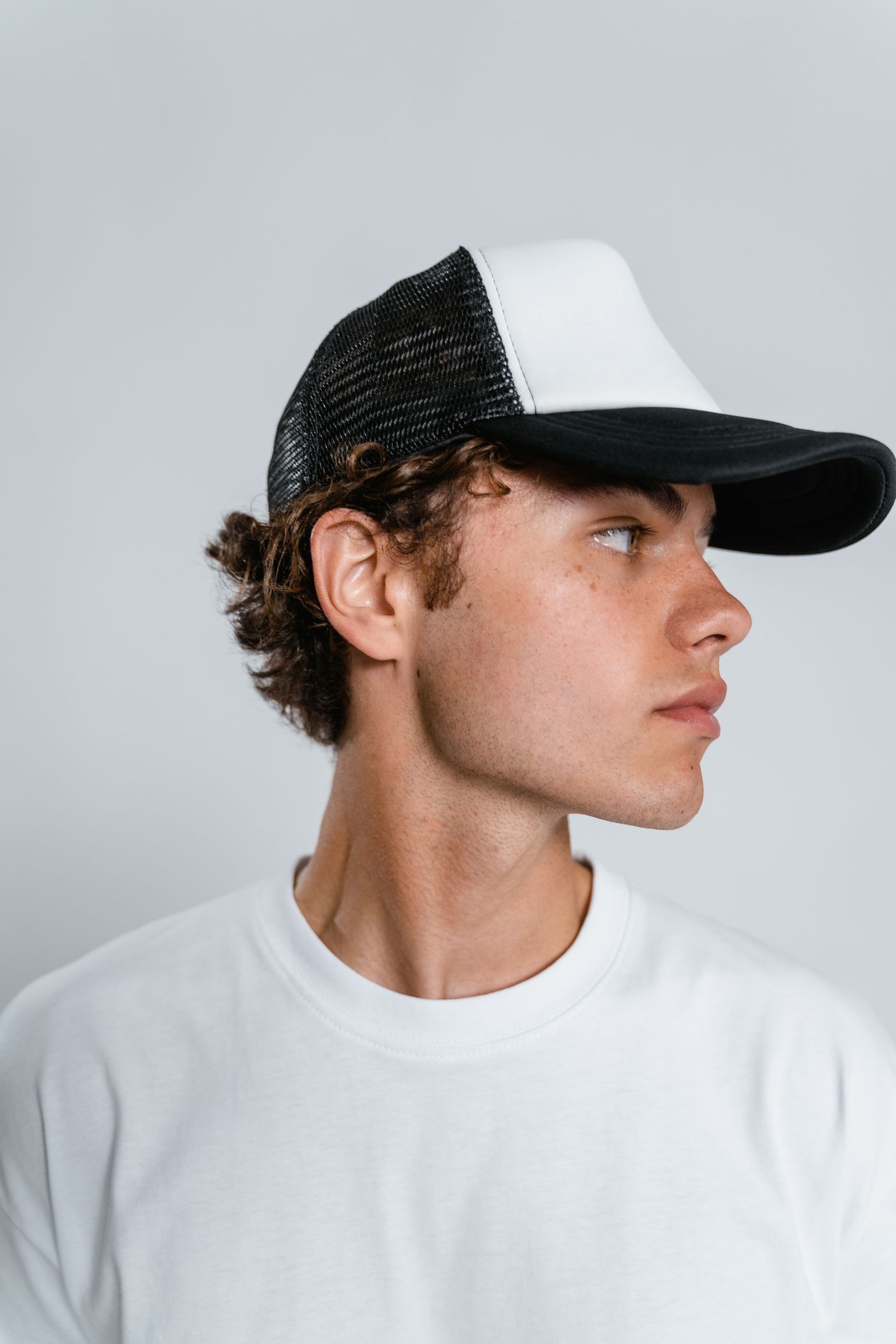 Side profile of a man wearing a black and white mesh trucker cap