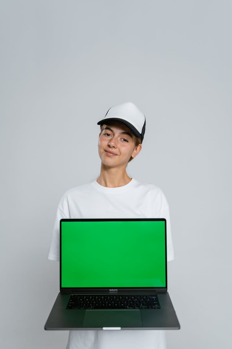 A Person Wearing A White Cap Behind A Laptop With Green Screen