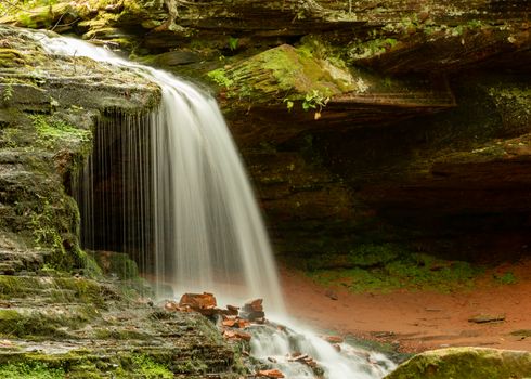 Calm waterfall cascading over rocks in a serene, green forest environment.