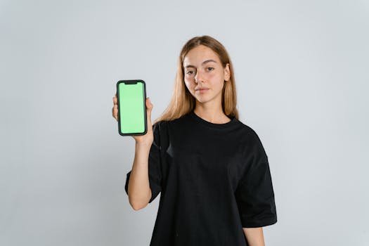 Young woman in black t-shirt holding a smartphone with a green screen, ideal for display mockup.