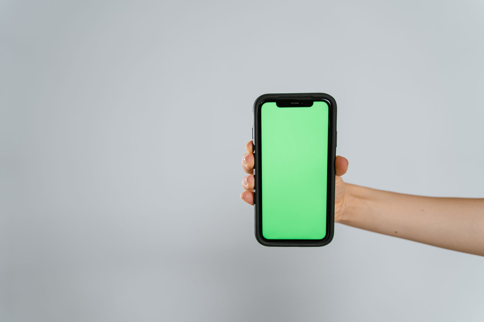 Close-up of a hand holding a smartphone with a green screen, offering ample copy space.