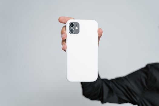 Close-up of a hand holding a smartphone with a white case against a plain background.