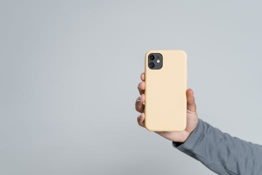 Person holding smartphone with pastel case against white background.