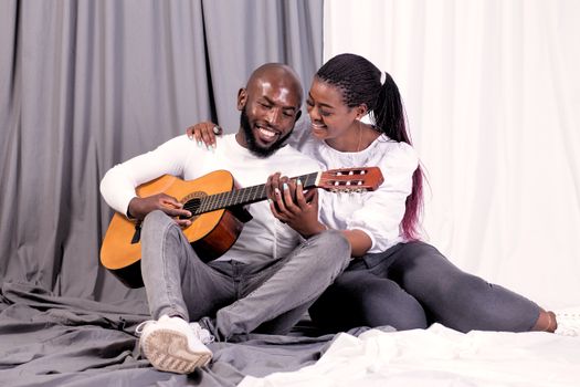 A joyful couple shares a musical moment with a guitar indoors.