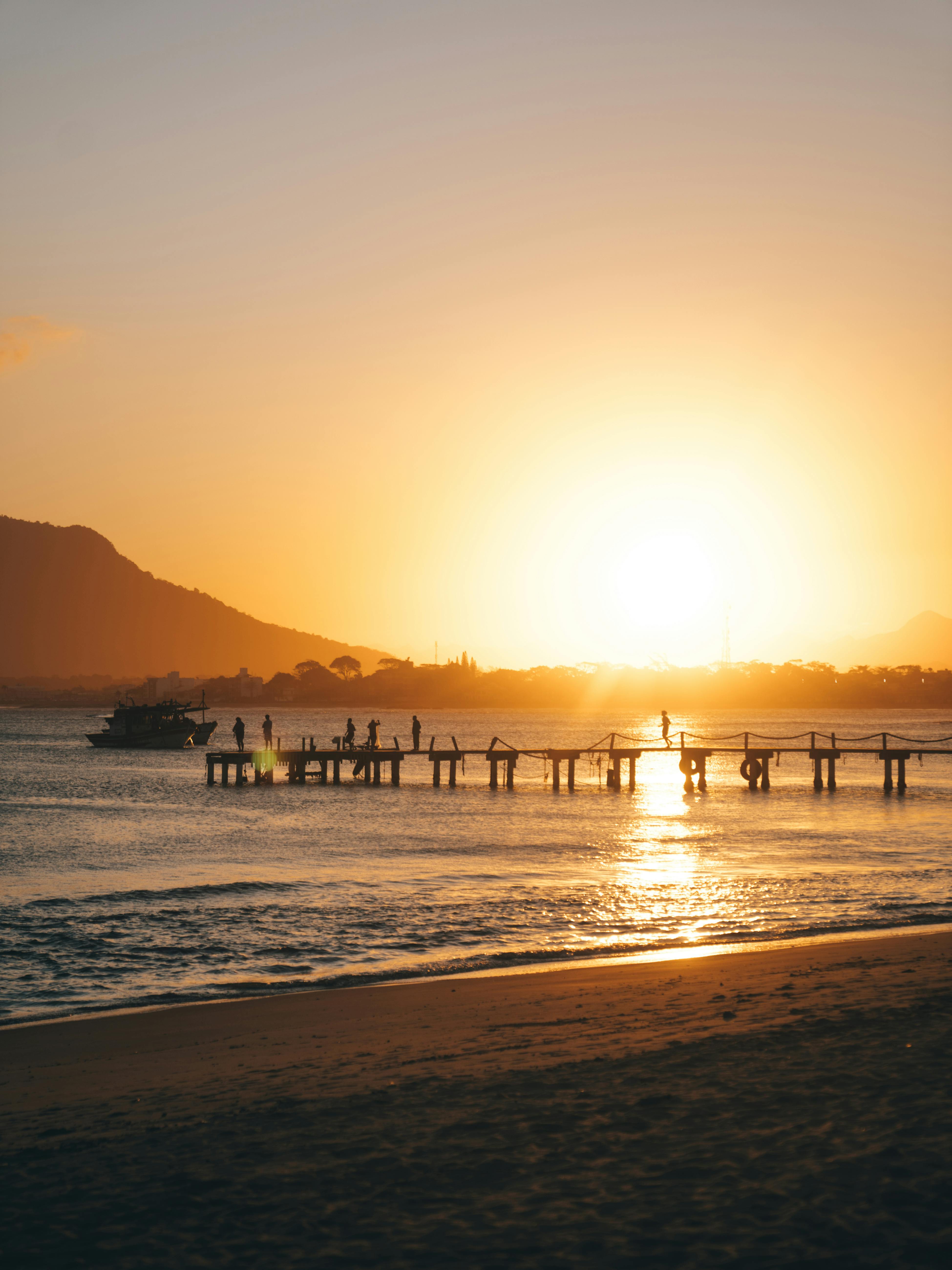 Scenic beach sunset with silhouetted dock and calm ocean waves.