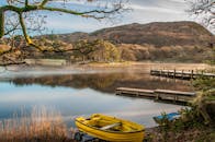 日出时分，湖面宁静，黄色的船、码头和山脉构成背景
