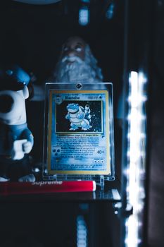 Blastoise Pokémon card in a protective case on display shelf with collectibles and ambient lighting.