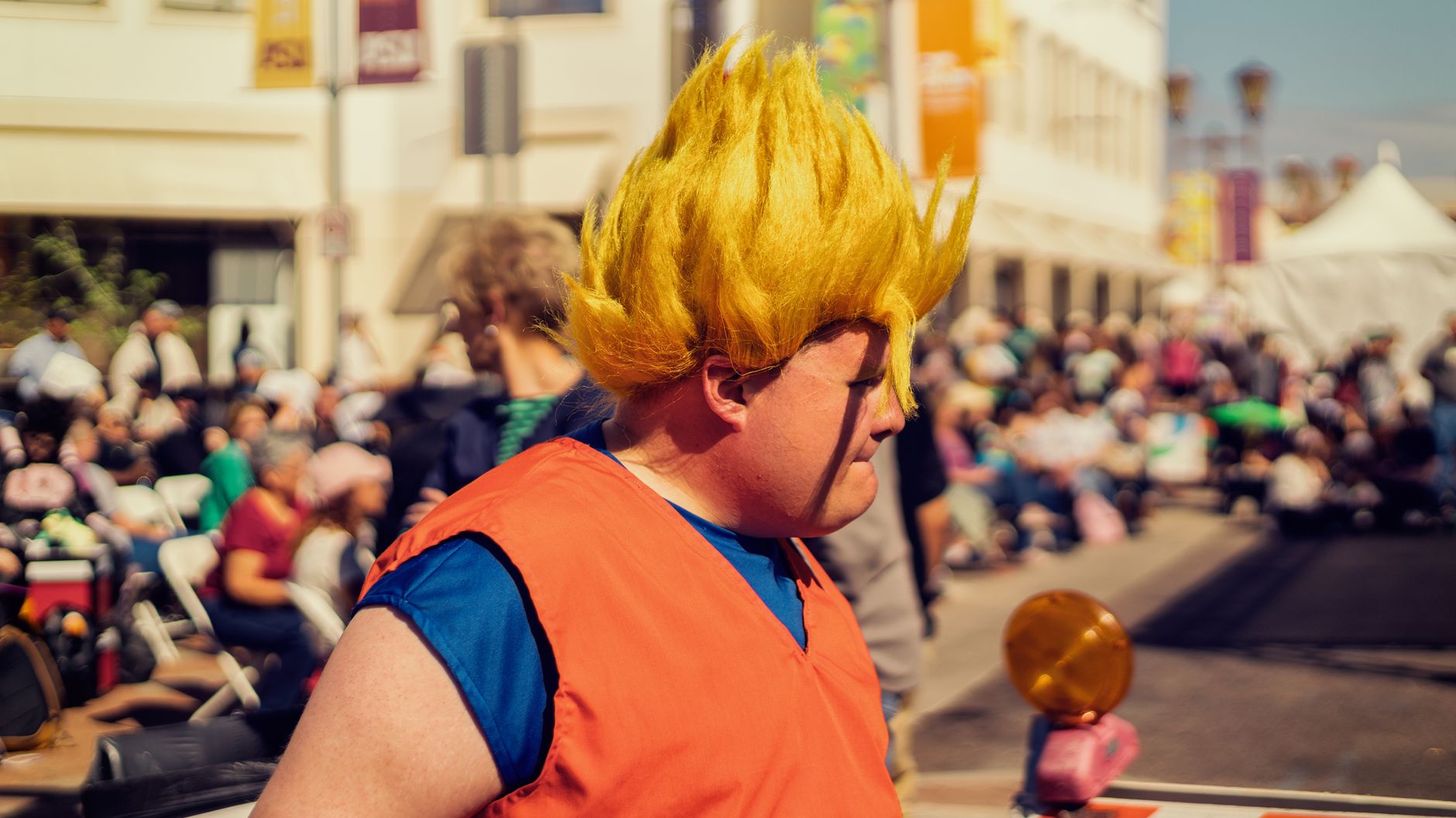 Man in Dragon Ball Z cosplay at a lively outdoor festival with a crowd in the background.
