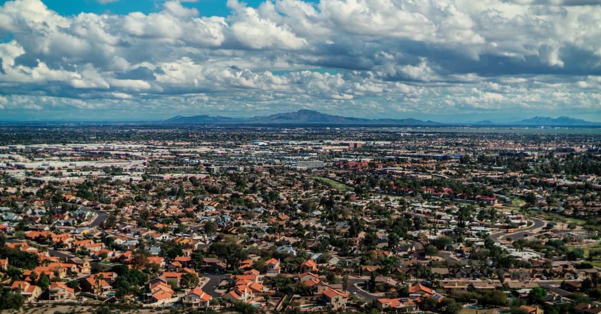 Aerial view of suburban rooftops under a cloudy sky with distant mountains in the background.