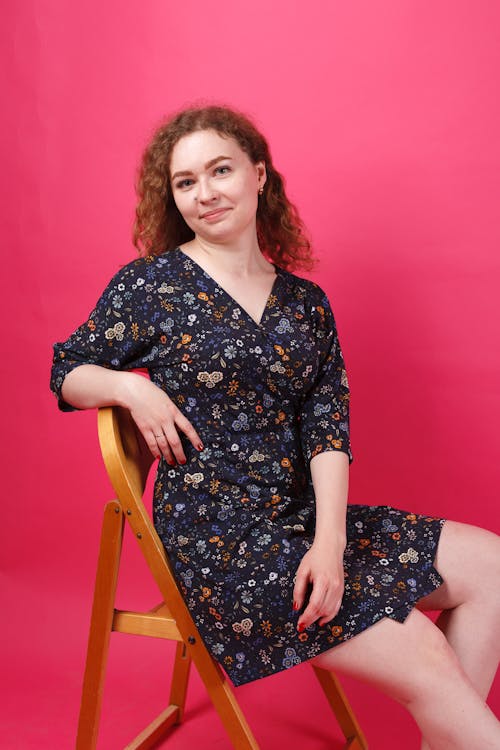 A Woman in a Floral Dress Sitting on a Wooden Chair 