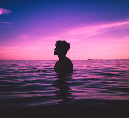 Silhouette of a Man in the Water During Pink Sky