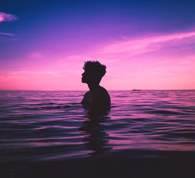 Silhouette of a person in the ocean at dusk with a vibrant pink sky in Toronto, Canada.