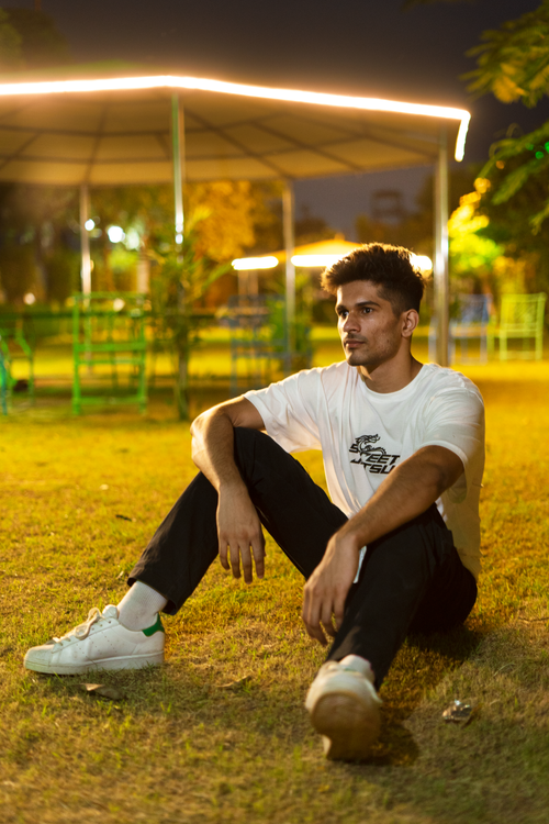 Free A young man in casual attire sits on the grass in a park at night, creating a relaxed and stylish atmosphere. Stock Photo