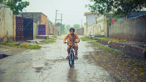 Free A Boy in Yellow Raincoat Riding Bicycle on a Dirt Road Stock Photo