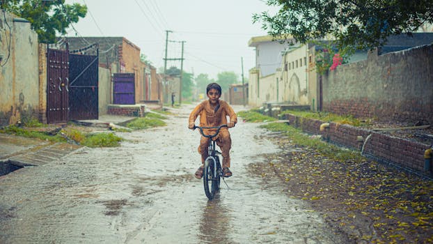 A young boy biking on a wet rural road during rainfall.