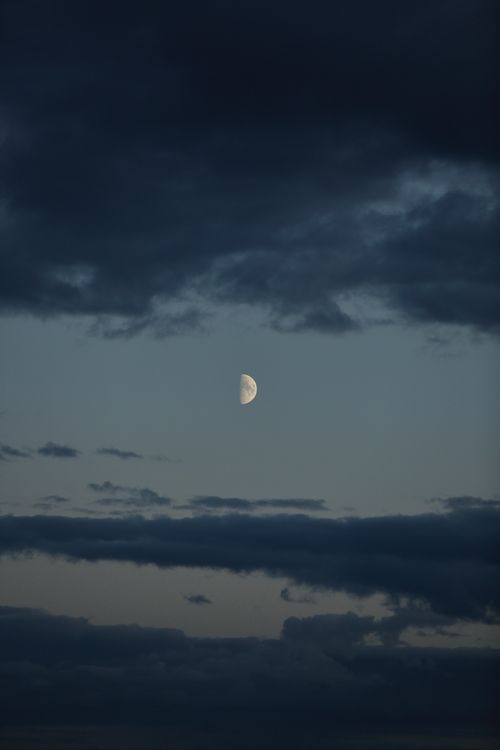 Free A calm half moon surrounded by dark clouds in the night sky, offering a tranquil view. Stock Photo