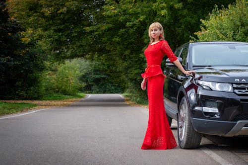 Beautiful Woman in Red Dress Standing Beside Black Car