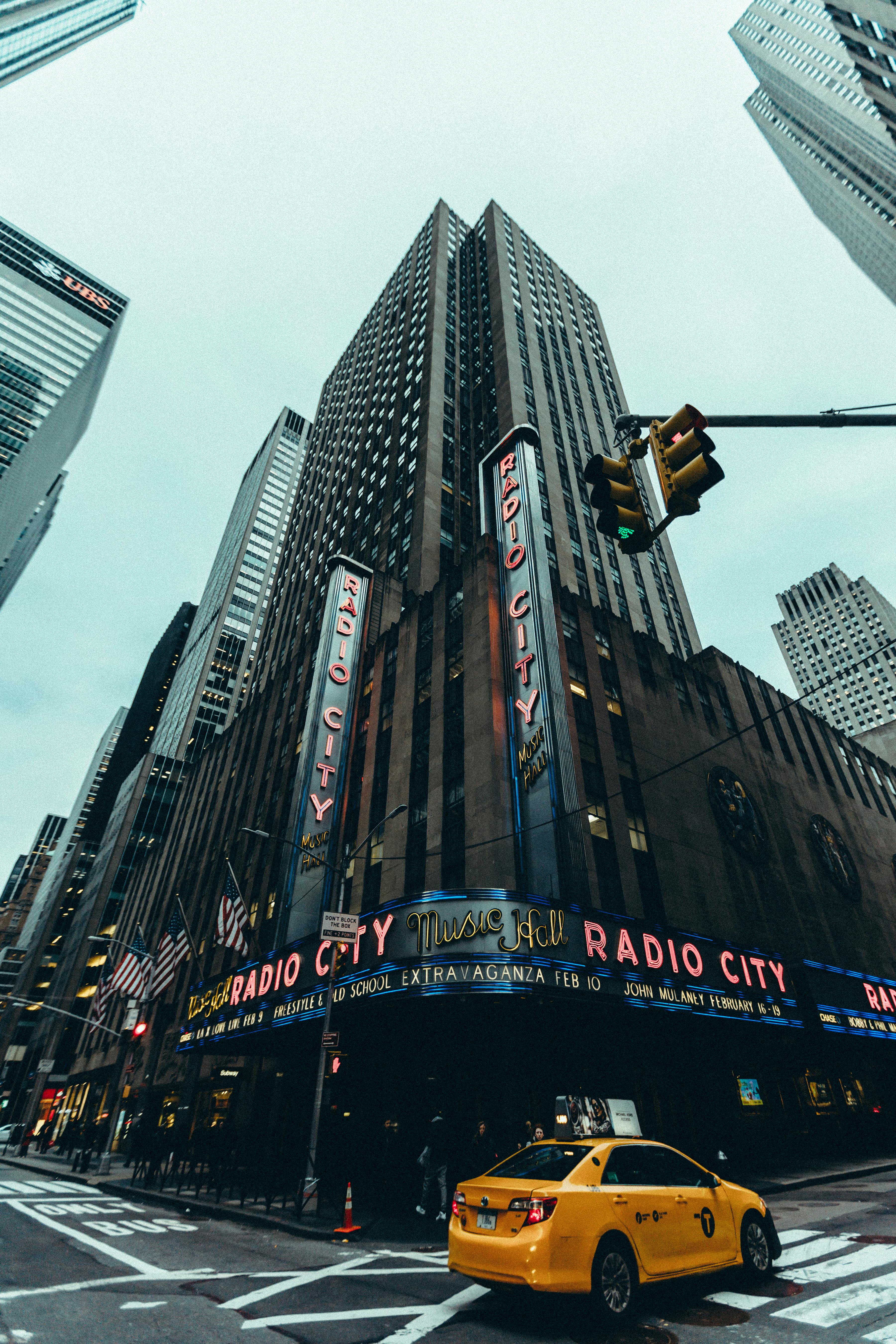 Free Dynamic city view of Radio City Music Hall with skyscrapers and yellow taxi in NYC. Stock Photo