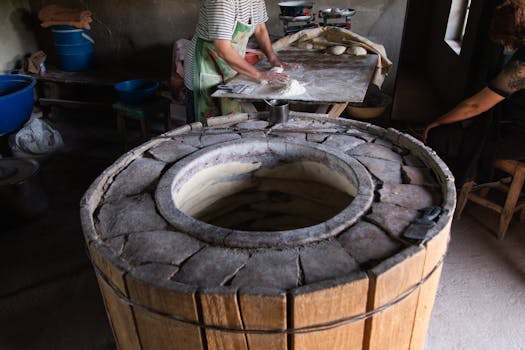 Man preparing dough beside a traditional tandoori oven in an authentic rustic kitchen.