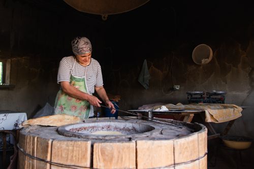 Free A woman baking traditional Georgian bread in a wood-fired oven indoors. Stock Photo