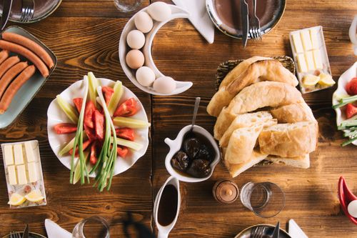 Free A beautifully arranged breakfast table with fresh bread, sausages, eggs, and vegetables. Stock Photo