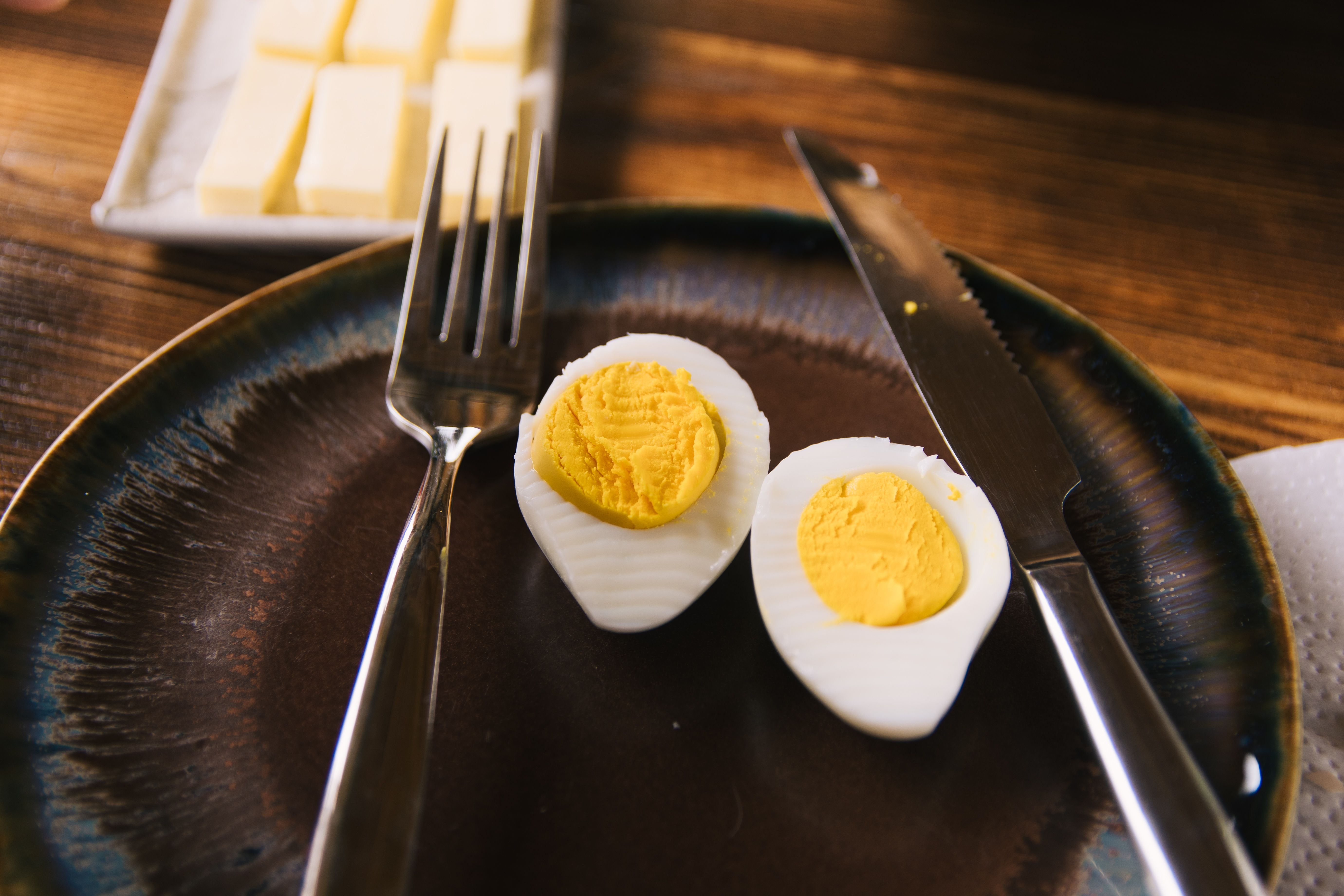 A close-up of a sliced hard boiled egg with a fork and knife on a rustic plate.