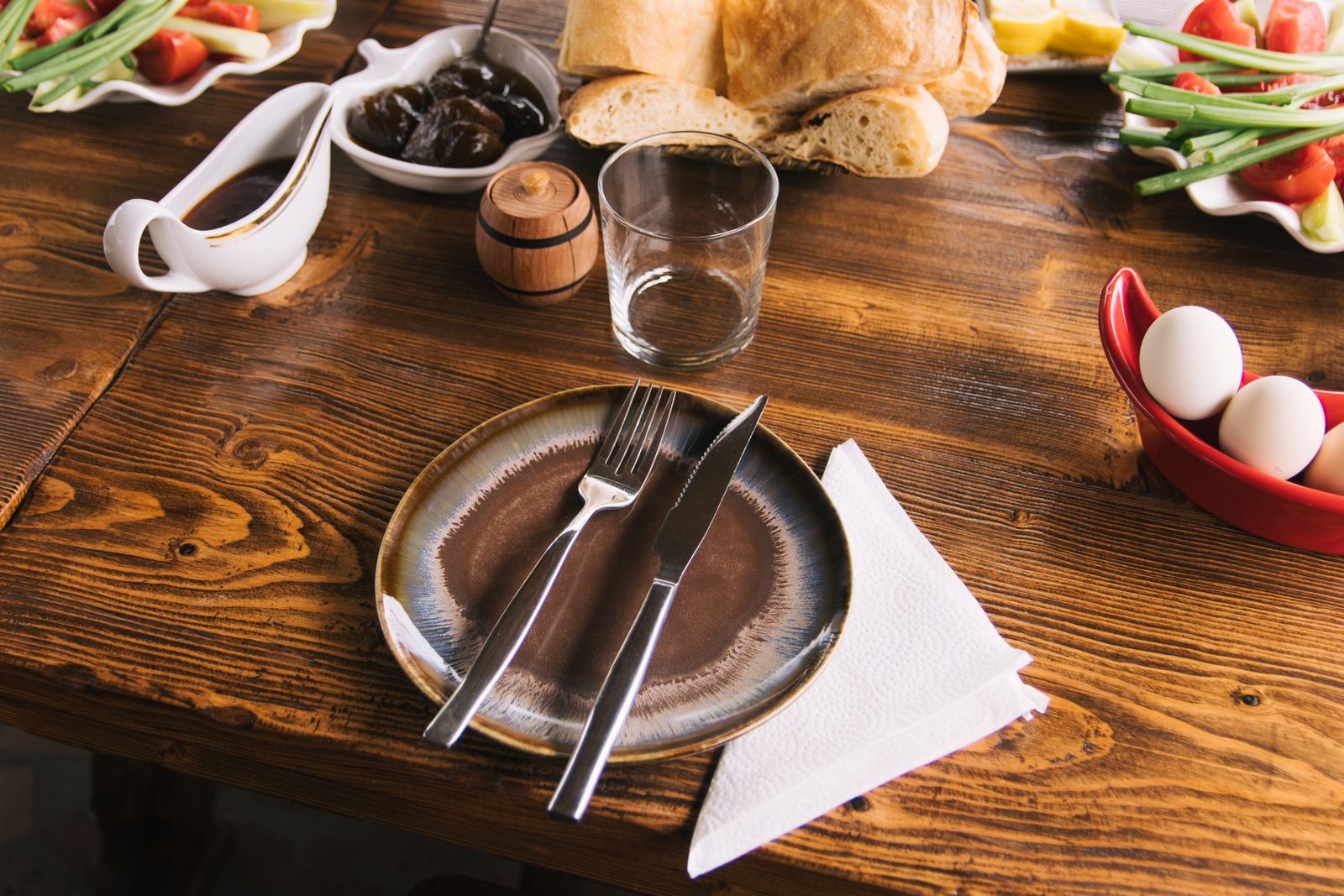 A rustic table setup with bread, veggies, and a ceramic plate for a cozy meal.