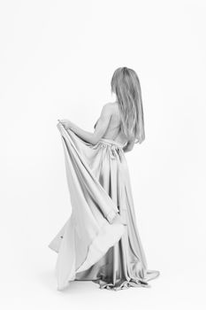 Black and white image of a woman in a backless long dress standing elegantly.
