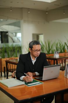 Focused businessman in black suit working on a laptop at a wooden table indoors. - Fotografer Sidoarjo