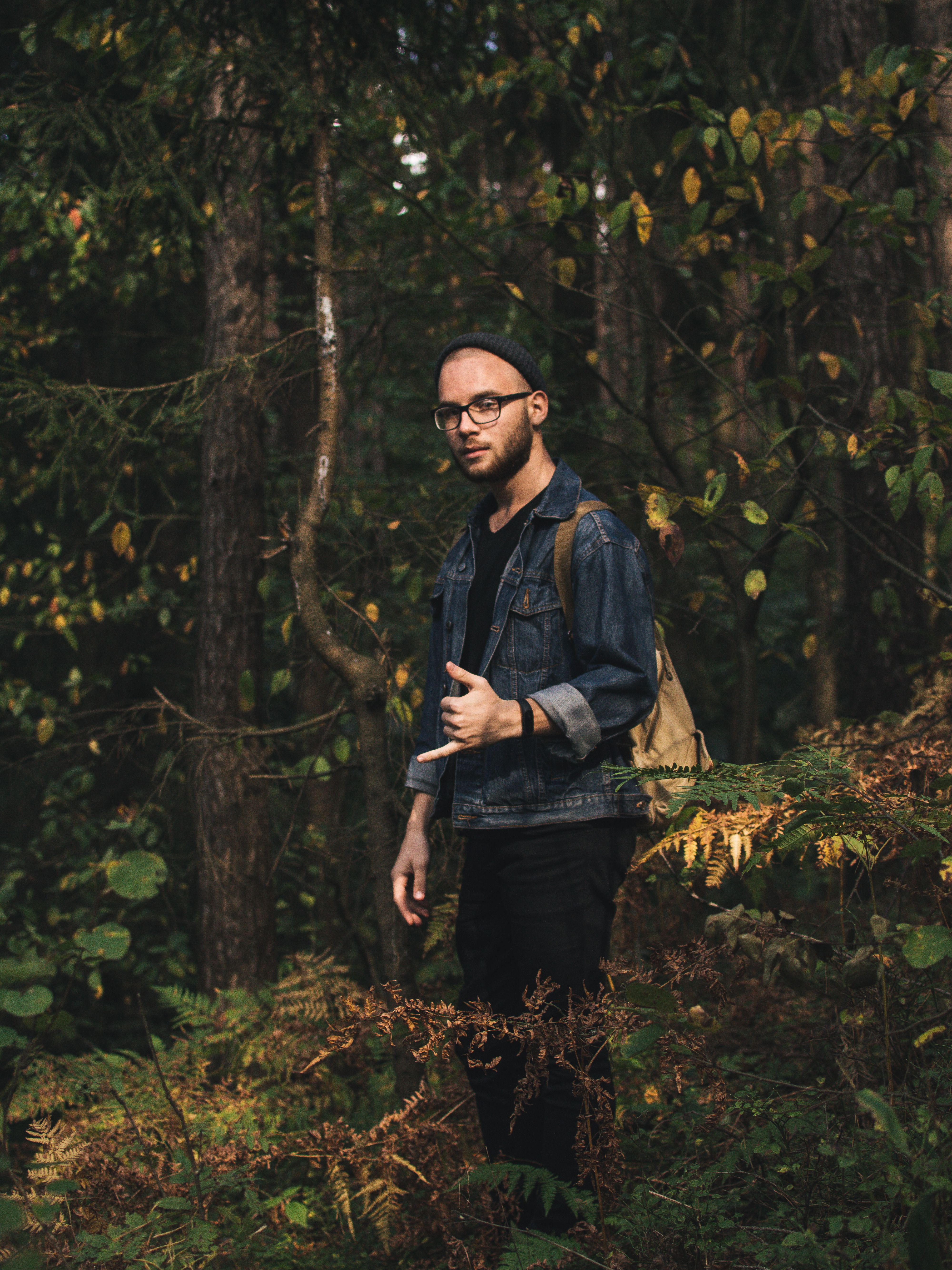 Stylish man with backpack and beanie posing during autumn forest adventure.