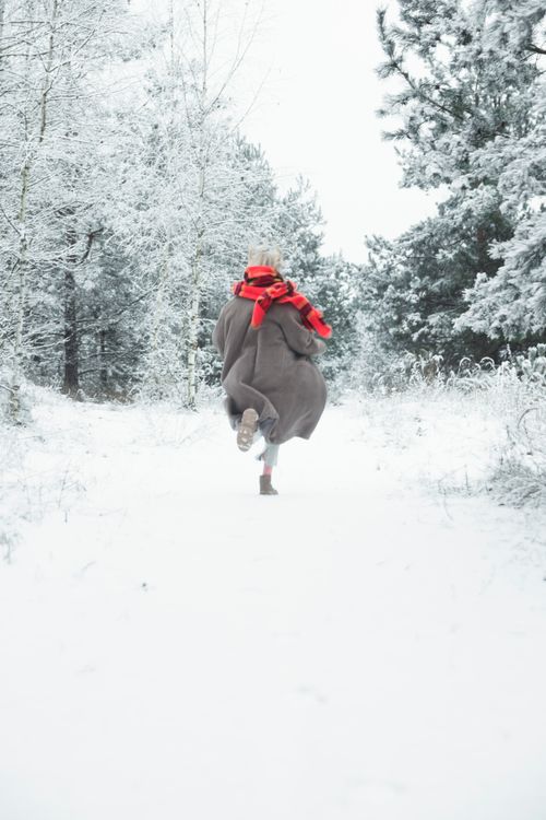 Free A person running alone in a snowy forest wearing a red scarf and coat. Stock Photo