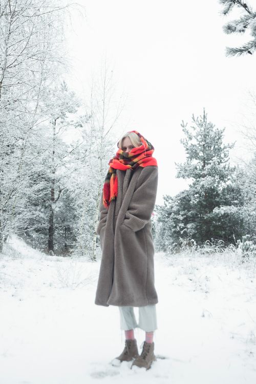 Free A woman wearing a long coat and scarf stands in a snow-covered forest. Stock Photo