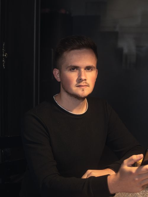 Free Portrait of a young man in dim light, wearing a black sweater, looking contemplative. Stock Photo